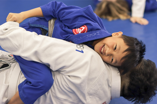 a boy smiling and practicing Jiu Jitsu with an adult at Gracie Barra Salt Lake City